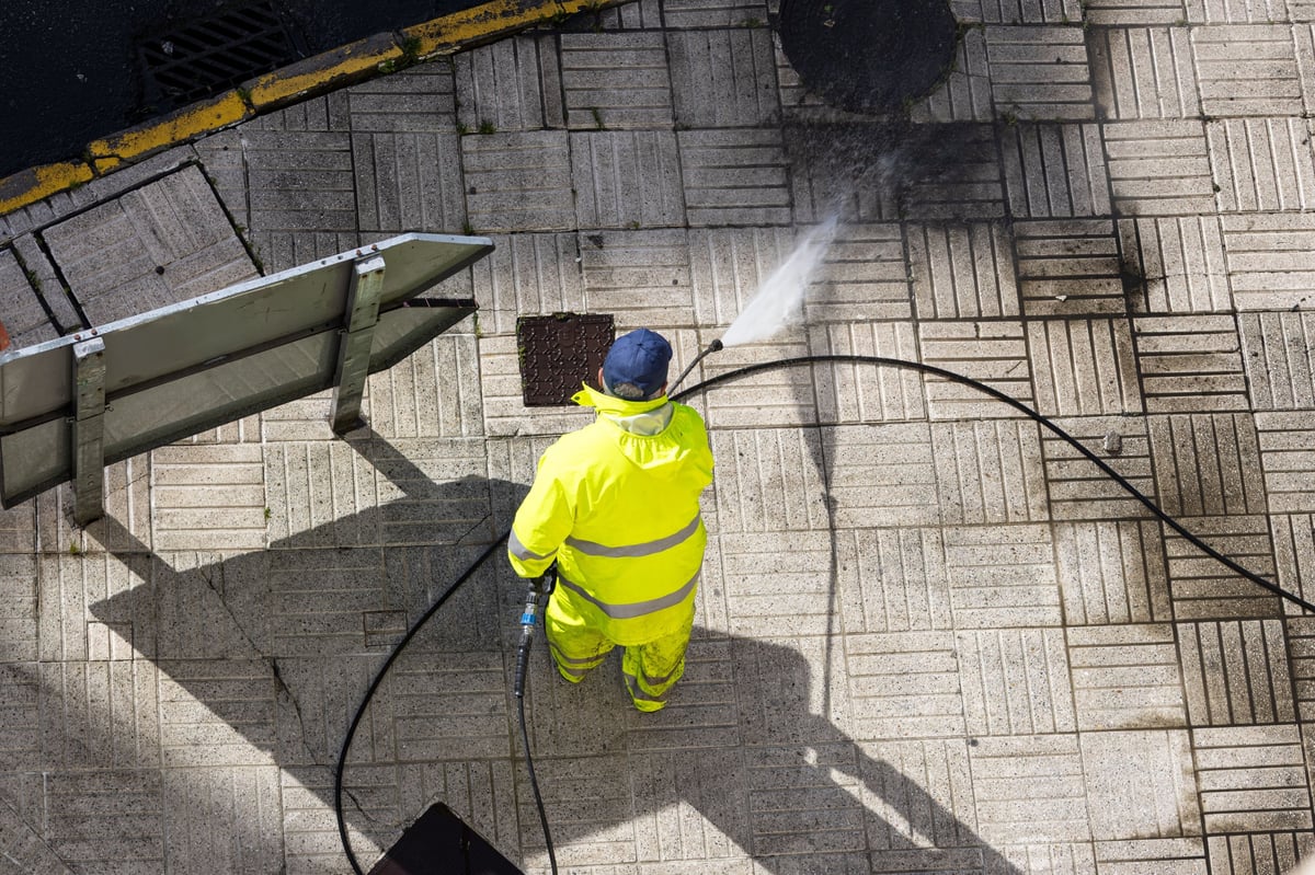 High-angle view of a JTR Services worker cleaning a sidewalk with a high-pressure water jet